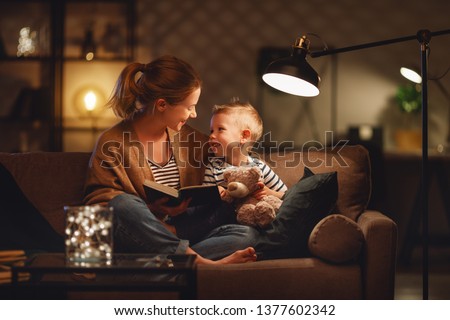 Family before going to bed mother reads to her child son book near a lamp in the evening