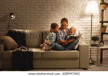 Family before going to bed mother reads children a book about a lamp in the evening