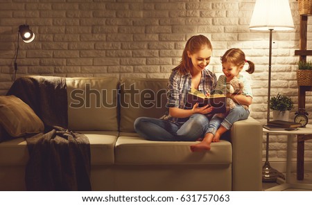 Family before going to bed mother reads to her child daughter book near a lamp in the evening