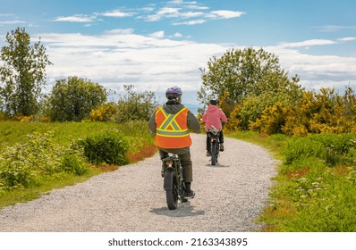 Family Bike Ride In Sunny Spring Day Along Fields And Forest. A Group Of Cyclists Riding On A Park Road. People Cycling On Trail Between The High Grass On An Embankment-May 29,2022-Delta BC Canada