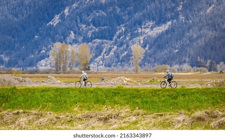 Family Bike Ride In Sunny Spring Day Along Fields And Forest. A Group Of Cyclists Riding On A Park Road. People Cycling On Trail Between The High Grass On An Embankment-April 24,2022-Langley BC Canada