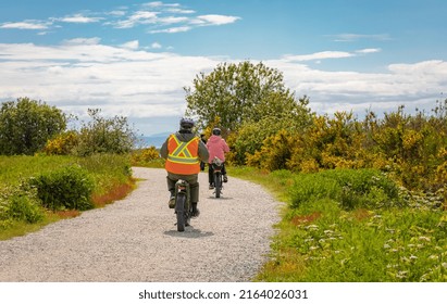 Family Bike Ride In Sunny Spring Day Along Fields And Forest. A Group Of Cyclists Riding On A Park Road. People Cycling On Trail Between The High Grass On An Embankment-May 29,2022-Delta BC Canada