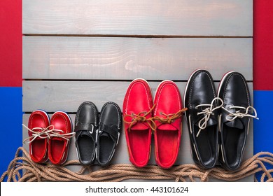 Family boat shoes on wooden background. Four pair of red and black boat shoes on grey desk with rope. Top view, copy space. family concept