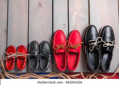 Family boat shoes on wooden background. Four pair of red and black boat shoes on grey desk with rope. Top view, copy space. family concept