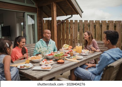 Family Bonding And Laughing, Sitting Having Breakfast Outside Holiday Cottage.