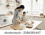 Family bonding through cooking. Happy loving young mom give culinary lesson to little schoolgirl daughter teach to knead roll dough help to use simple kitchen utensils to cook homemade bakery treats