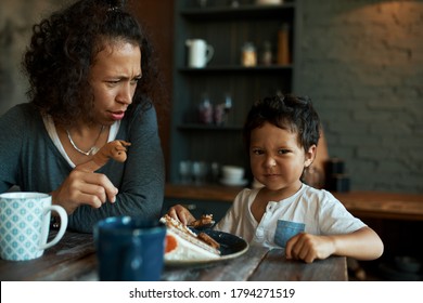 Family Breakfast. Indoor Image Of Dark Skinned Young Female With Finger Puppet Trying To Entertain Her Stubborn Baby Son Sitting At Dining Table, Eating Cake And Drinking Tea. Parenting And Maternity