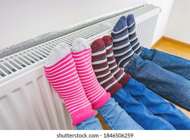 A family in bright warm winter socks warms their feet on the heating radiator in the house. Electric or gas heater at home. The symbolic image of the heating season at home. - Shutterstock ID 1846506259