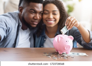 Family Budget. Happy Black Couple Putting Money Cash To Piggybank, Making Savings For Future, Sitting Together At Home