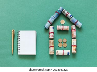 Family budget planning concept. Money to buy a home. Loan for building a house. Symbolic house made of twisted euro banknotes and a notebook with a pen on a green background