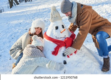 Family Builds Snowman Together In Winter In The Park