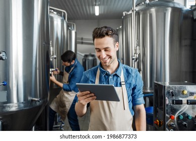 Family business, brewers working in craft beer brewery, control production. Smiling millennial handsome man in apron use tablet, guy check data on large metal tank with craft drink, empty space - Powered by Shutterstock