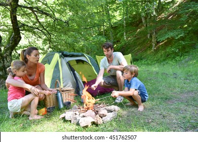 Family Camping And Cooking Sausages In Campfire