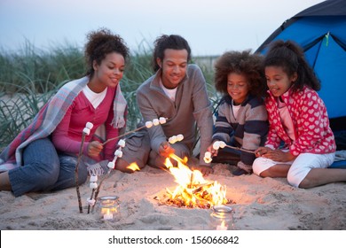 Family Camping On Beach And Toasting Marshmallows