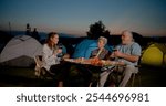 Family camping together at sunset in the park with smiles and love, having a barbeque and cooking food enjoying nature and leisure outdoors during summer