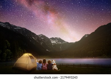 Family camping under starry night sky. Milky way watching. Camp bonfire with kids. Travel and hiking with young children and dog. Group of people next to tent in national park. Star gazing. - Shutterstock ID 2179493243