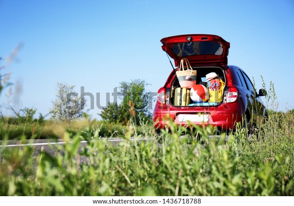 Family car with open trunk full of luggage on\
highway. Space for text