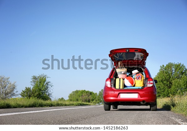 Family car with open trunk full of luggage on
highway. Space for text