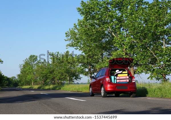 Family car with open trunk full of luggage on\
highway. Space for text