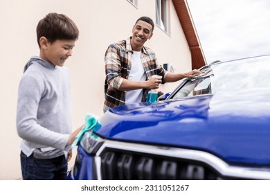 Family car wash. Happy father and his son cleaning automobile together, boy wiping spotlight while dad washing car windshield with rag and spray - Powered by Shutterstock