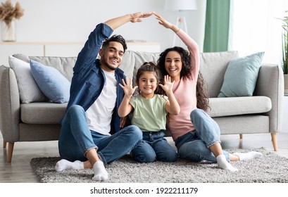 Family care. Arabic parents making symbolic roof of hands above cute little daughter while sitting together on floor in living room, middle eastern mom and dad having fun with their child at home - Powered by Shutterstock