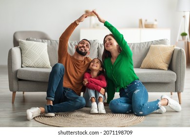 Family Care. Arabic parents making symbolic roof of hands above cute little daughter while sitting together on floor in living room, Middle Eastern mom and dad having fun with their child at home - Shutterstock ID 2071198709