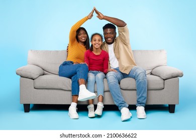 Family Care, Protection And Insurance Concept. Portrait of smiling young African American parents making symbolic roof of hands above their happy daughter sitting on sofa couch at blue studio wall - Shutterstock ID 2100636622