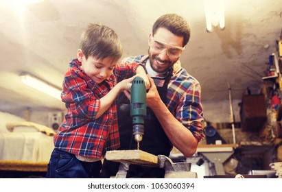 family, carpentry, woodwork and people concept - father and little son with drill perforating wood plank at workshop