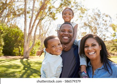 Family Carrying Children On Shoulders As They Walk In Park