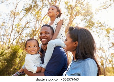 Family Carrying Children On Shoulders As They Walk In Park