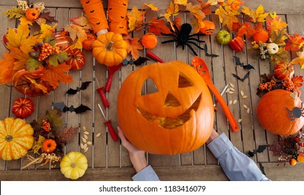 Family carving Halloween pumpkin on wooden table with autumn leaves decoration. Top view flat lay of hands and carved pumpkins. Halloween trick or treat. Seasonal home décor.