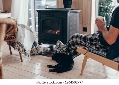 Family and cat relaxing in armchair by the fire place in wooden cabin. Warm and cozy winter holiday concept.