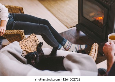 Family And Cat Relaxing In Wicker Armchair By The Fire Place In Wooden Cabin. Warm And Cozy Winter Holiday Concept.