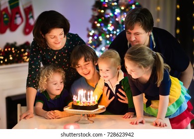 Family Celebrating Birthday And Christmas. Child Born On Xmas Eve Blowing Candles On Cake. Mother, Father And Kids Eating New Year Dessert. Parents And Children Opening Christmas Presents.