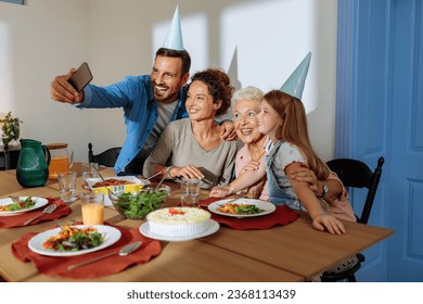 Family celebrating grandmas birthday with birthday cake and hats, taking a selfie during lunch and having a great time - Powered by Shutterstock