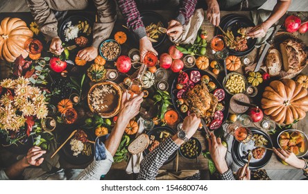 Family celebrating Thanksgiving day. Flat-lay of eating and pouring wine peoples hands over Friendsgiving table with traditional Fall food, roasted turkey, candles, pumpkin pie, top view