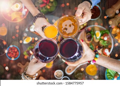 Family Celebration Dinner For Christmas With Wine And Beer, Cheers With Hands. Top View Of Hands At The Dinner Table At The Restaurant With Lots Of Tapas 