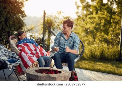 Family celebration of Independence Day. In the atmosphere of warmth and joy, the daughter coverd herself with American flag, symbolizing their deep-rooted American pride and patriotism. - Powered by Shutterstock