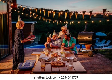 Family Celebration Outside In The Backyard. Big Garden Party. Birthday Party. Young Adult Woman Brings Birthday Cake.