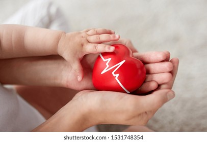 family, charity and health concept - close up of little baby and mother's hands holding red heart with ecg line - Powered by Shutterstock