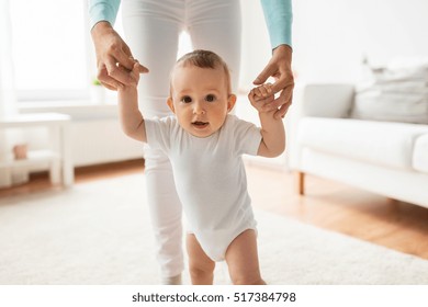 Family, Child, Childhood And Parenthood Concept - Happy Little Baby Learning To Walk With Mother Help At Home