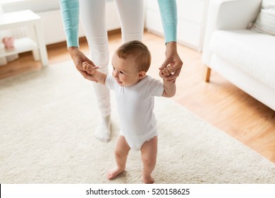 Family, Child, Childhood And Parenthood Concept - Happy Little Baby Learning To Walk With Mother Help At Home