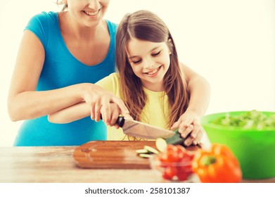 Family, Child, Cooking And Home Concept - Smiling Little Girl With Mother Chopping Cucumber In The Kitchen