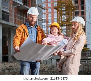 Family With Child Studying Architectural Drawings Outside Apartment Building Under Construction. Man And Woman Discussing Building Plan While Standing With Kid At Construction Site.