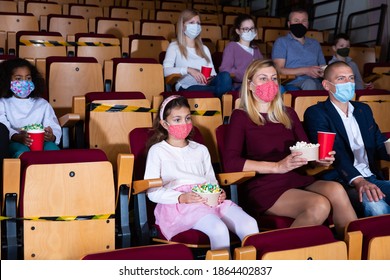 Family with child wearing protective masks eating popcorn and watching a movie in the cinema - Powered by Shutterstock