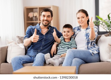family, childhood and fatherhood concept - portrait of happy father, mother and little son sitting on sofa and showing thumbs up at home - Shutterstock ID 1398230018
