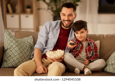 family, childhood, fatherhood, technology and people concept - happy father and little son with popcorn watching tv at home in evening