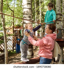 Family With Children In The Amusement Park. Mom Helps The Baby Stay On The Obstacle Course