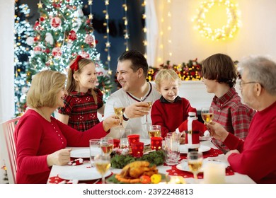 Family with children eating Christmas dinner at fireplace and decorated Xmas tree. Parents, grandparents and kids at festive meal. Winter holidays celebration and food. Kids open presents and gifts. - Powered by Shutterstock