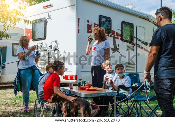 A family with children having a snack next\
to their motorhome at a service\
area
